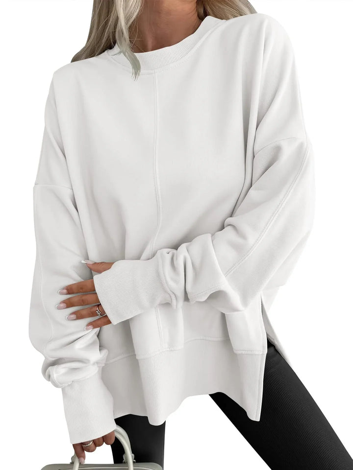 Woman wearing oversized white sweatshirt with ribbed cuffs and black leggings holding a light handbag