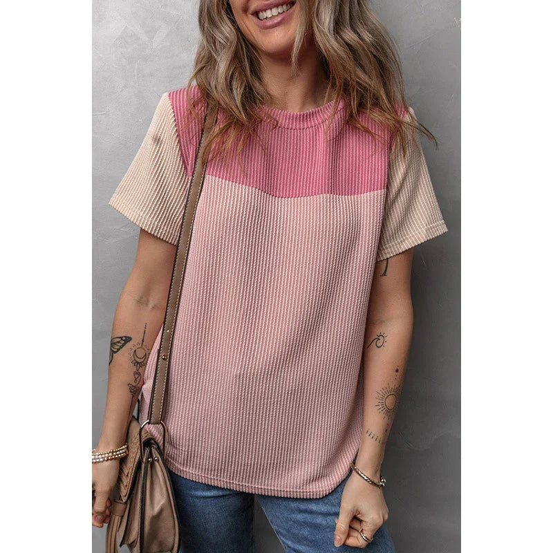 Woman wearing a colorblock pink and beige short sleeve knit top with blue jeans and a brown shoulder bag