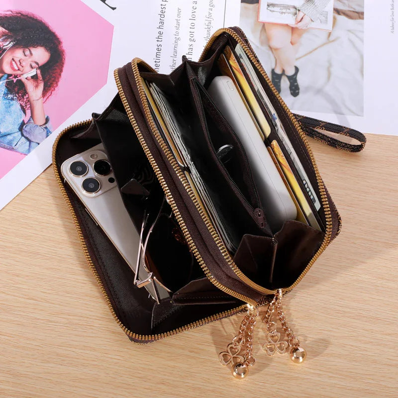 Open black leather zippered wallet with gold charms, holding smartphone, sunglasses, cards on wooden surface