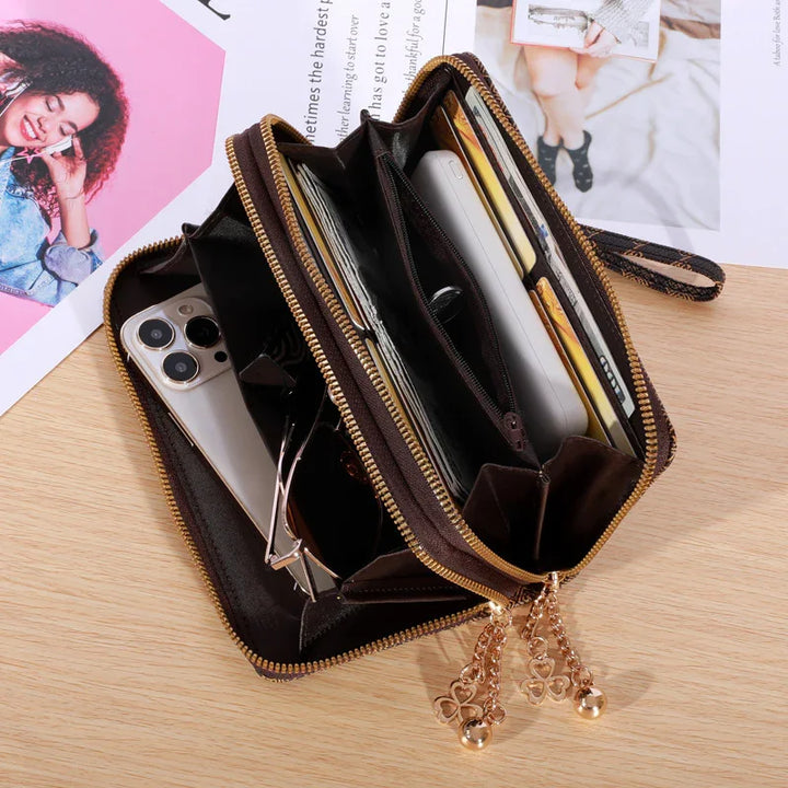 Open black leather zippered wallet with gold charms, holding smartphone, sunglasses, cards on wooden surface