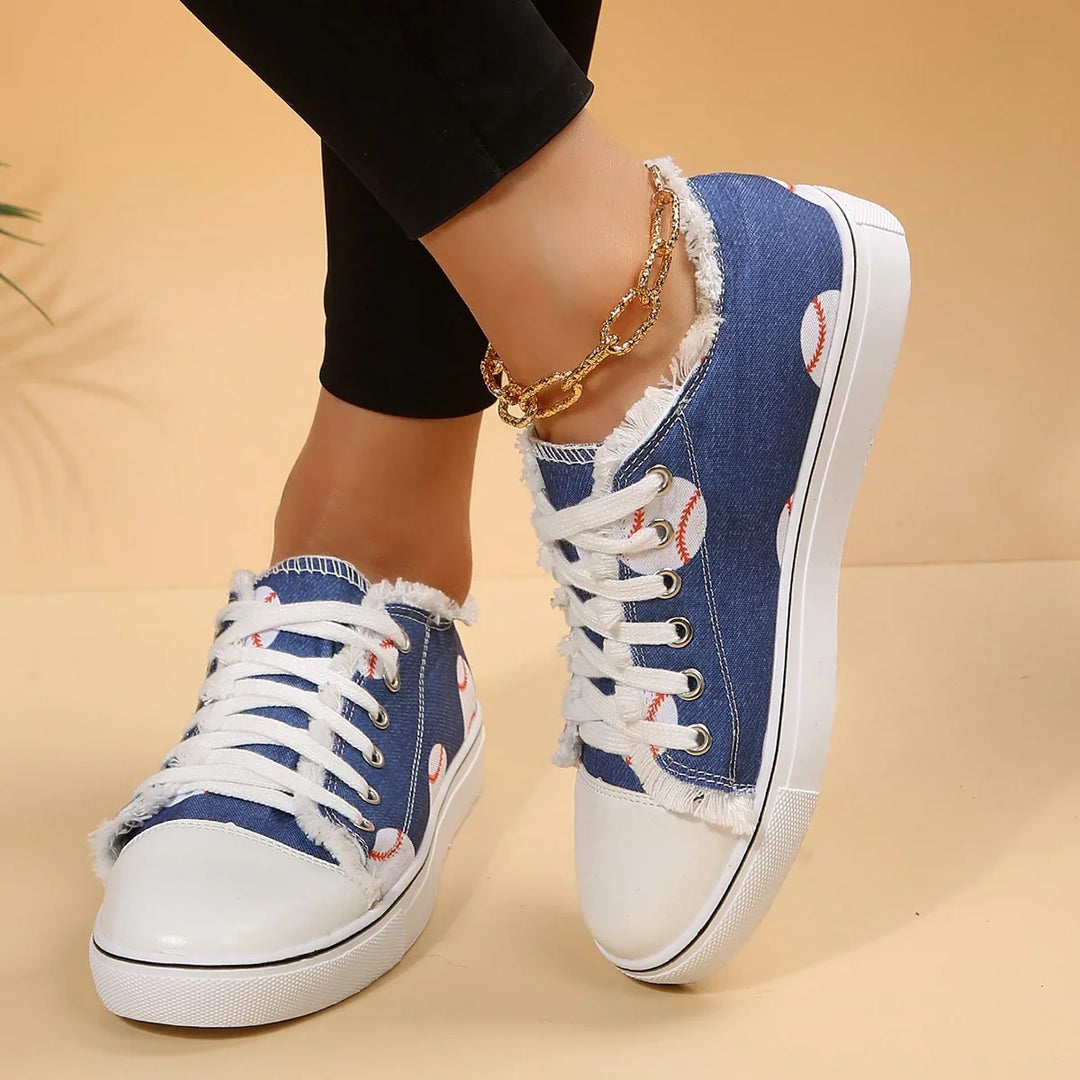 Casual blue denim sneakers with white baseball pattern and frayed edges worn with black pants and gold anklet
