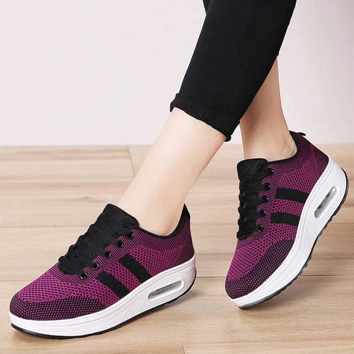 Pair of purple and black knit platform sneakers with white air-cushioned soles worn with black pants