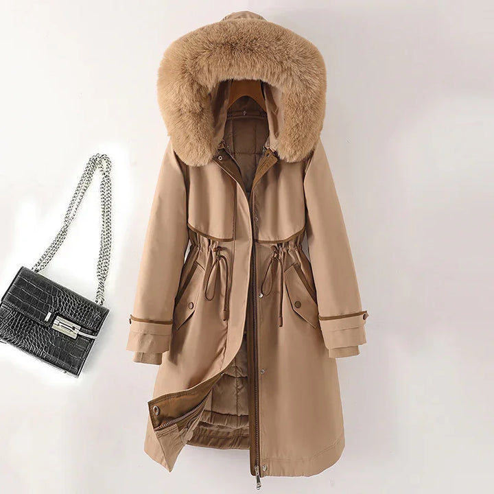 Beige winter coat with large fur-trimmed hood and drawstring waist next to black chain-strap handbag