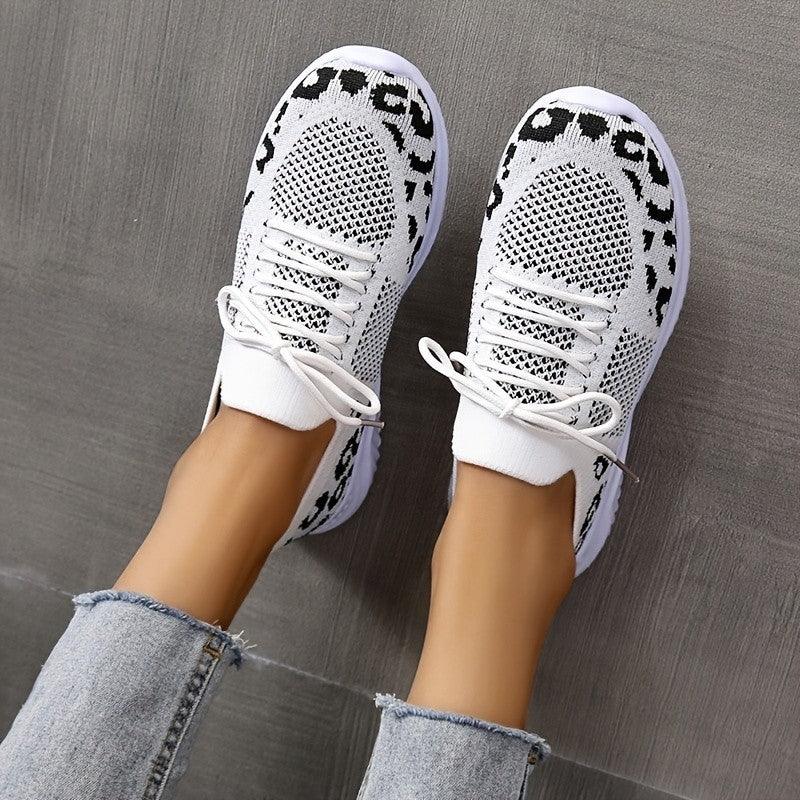 Top view of white and black knit sneakers worn with light blue frayed hem jeans on gray floor