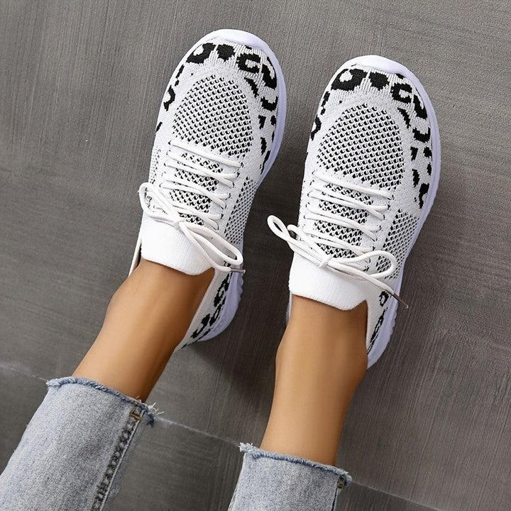 Top view of white and black knit sneakers worn with light blue frayed hem jeans on gray floor