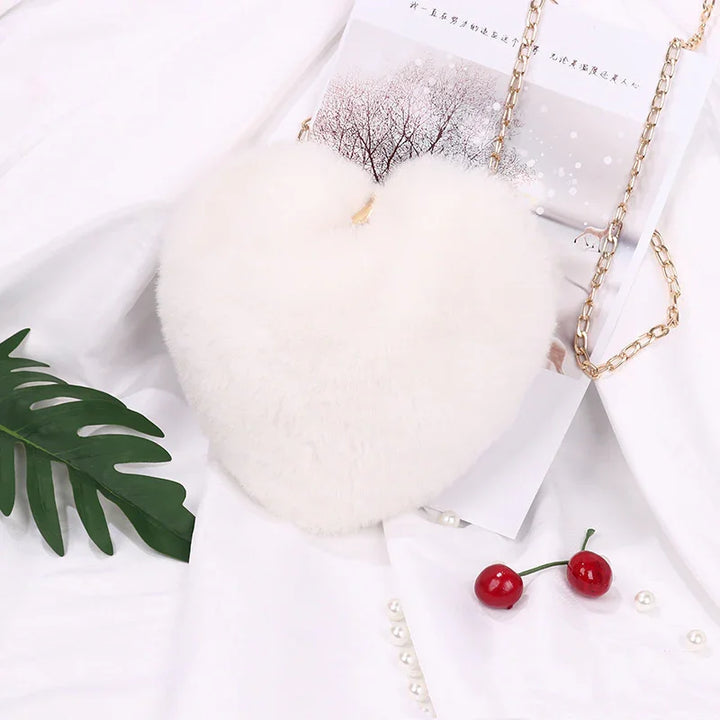 White fluffy heart-shaped handbag with gold chain strap on white fabric with cherries and green leaf