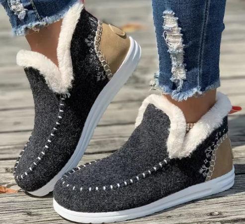 Cozy dark gray fleece-lined slip-on shoes with white stitching and tan heel detail worn with ripped jeans