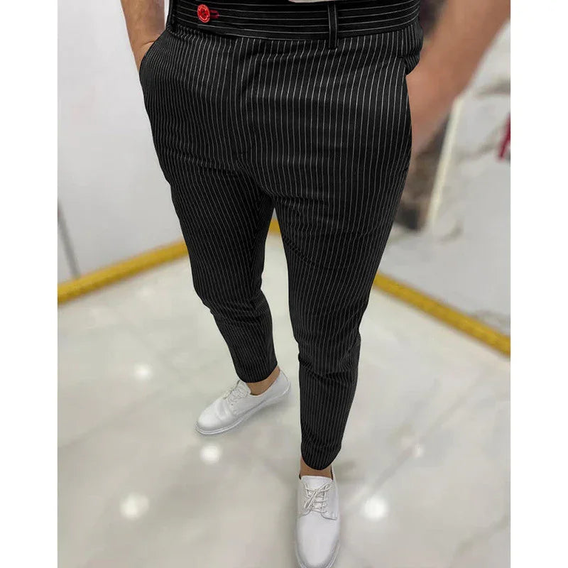 Man wearing black pinstripe trousers with red button detail and white dress shoes on marble floor