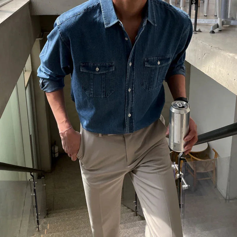 Person wearing blue denim shirt and beige pants holding a silver can while walking up stairs indoors