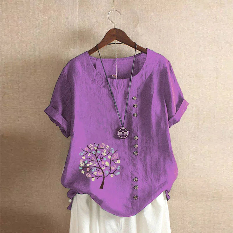 Purple short sleeve blouse with front buttons and tree print paired with white pants on wooden hanger