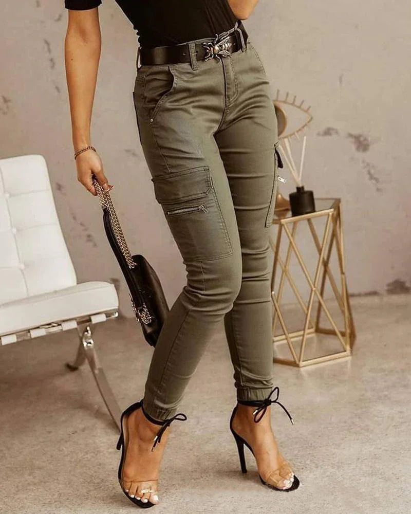 Woman wearing olive green cargo pants with black belt and transparent high heels in a modern minimalist room