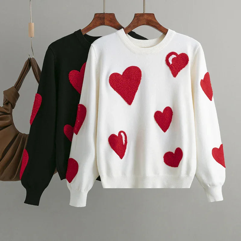 White and black sweaters with red heart patterns hanging on wooden hangers against gray background