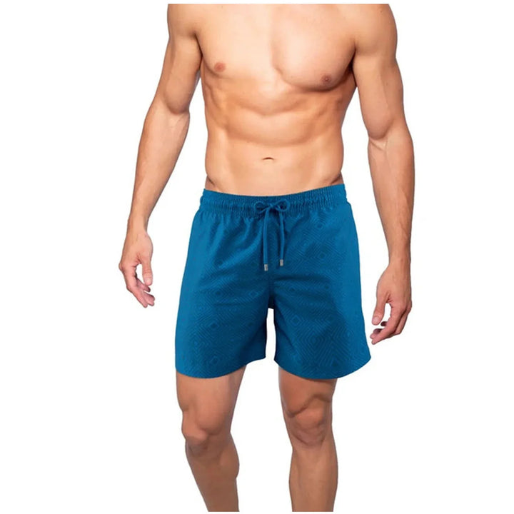 Male model wearing blue swim shorts with a subtle geometric pattern, elastic waistband, and drawstring