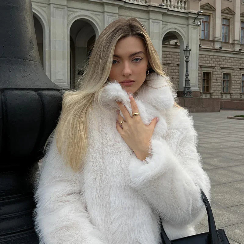 Blonde woman wearing a white faux fur coat standing outdoors near historic building with arches