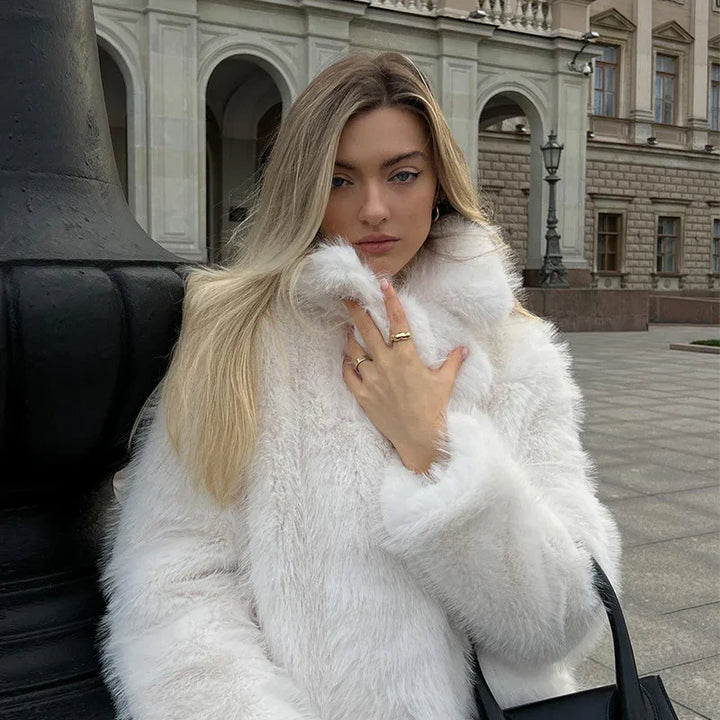 Blonde woman wearing a white faux fur coat standing outdoors near historic building with arches