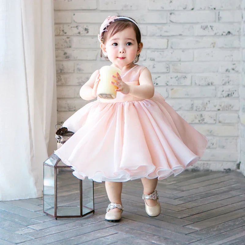 Toddler girl in pink fluffy dress holding a large candle, standing on gray floor with lantern and white brick wall background