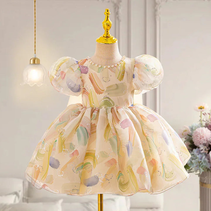 Pastel watercolor print baby dress with puff sleeves on gold mannequin in elegant room