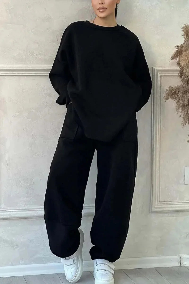 Woman wearing black oversized sweatshirt and pants with white sneakers against textured beige wall