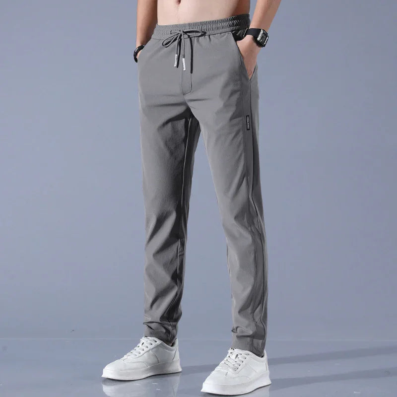 Man wearing gray jogger pants with drawstring waist and white sneakers on gray background
