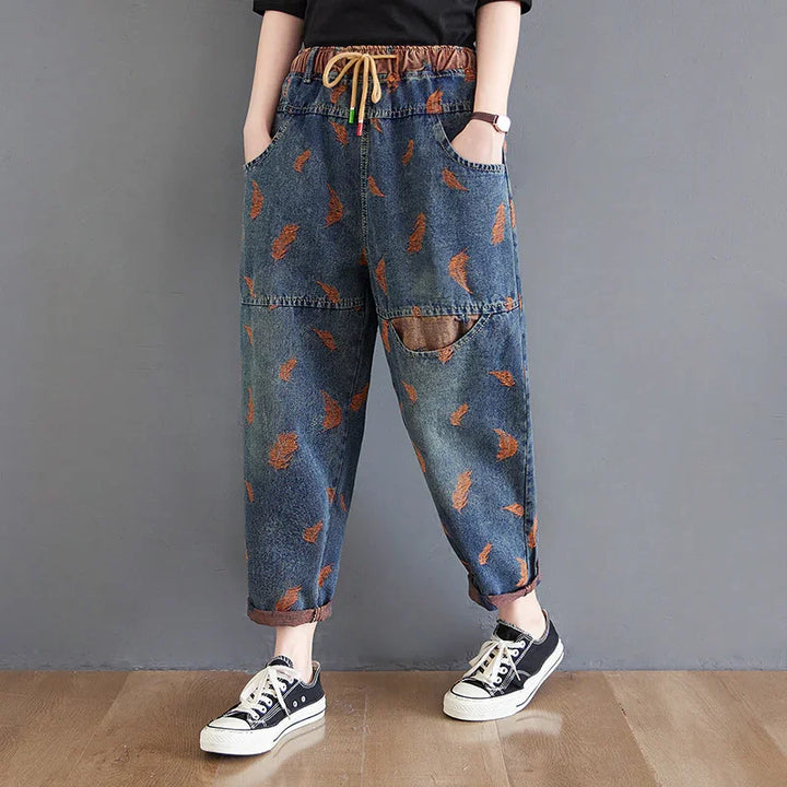 Casual denim pants with orange leaf patterns, elastic waistband, hands in pockets, black sneakers