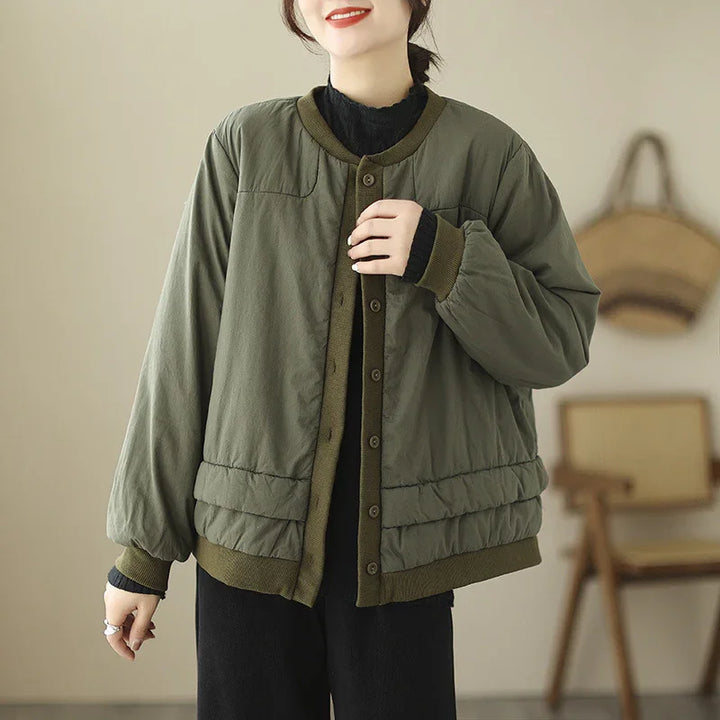 Woman wearing olive green button-up padded jacket with ribbed cuffs and hem in cozy indoor setting