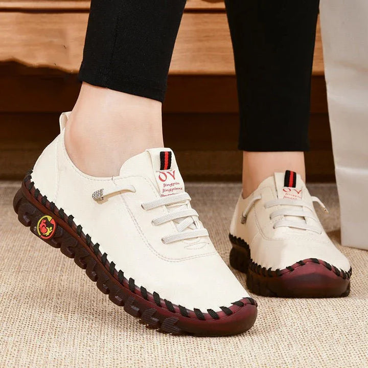 White casual leather shoes with black and red sole stitching on beige carpet