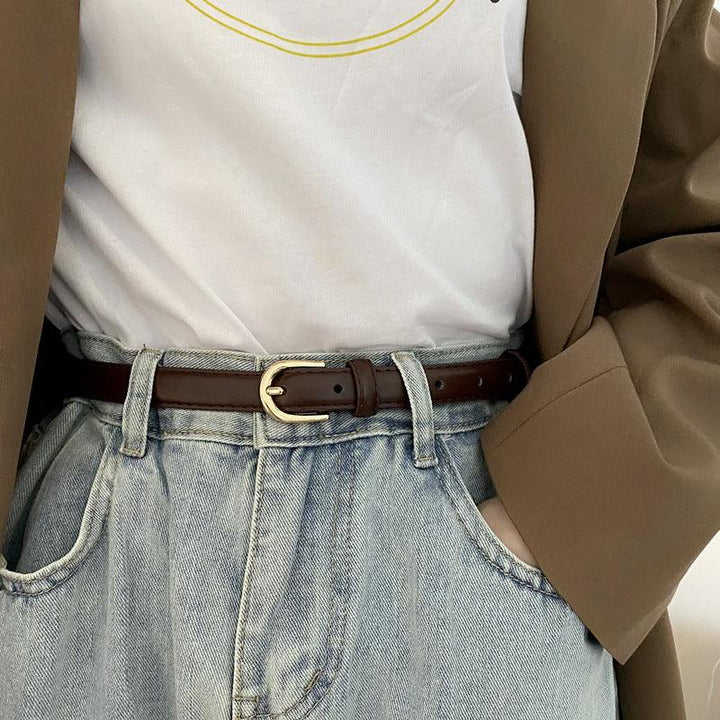 Close-up of person wearing light blue high-waisted jeans, brown leather belt with gold buckle, white t-shirt, and brown blazer