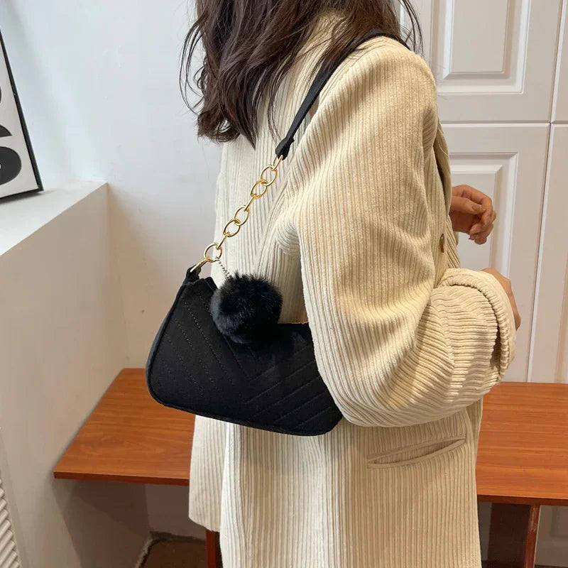 Woman wearing cream corduroy jacket with black quilted shoulder bag featuring gold chain and pompom