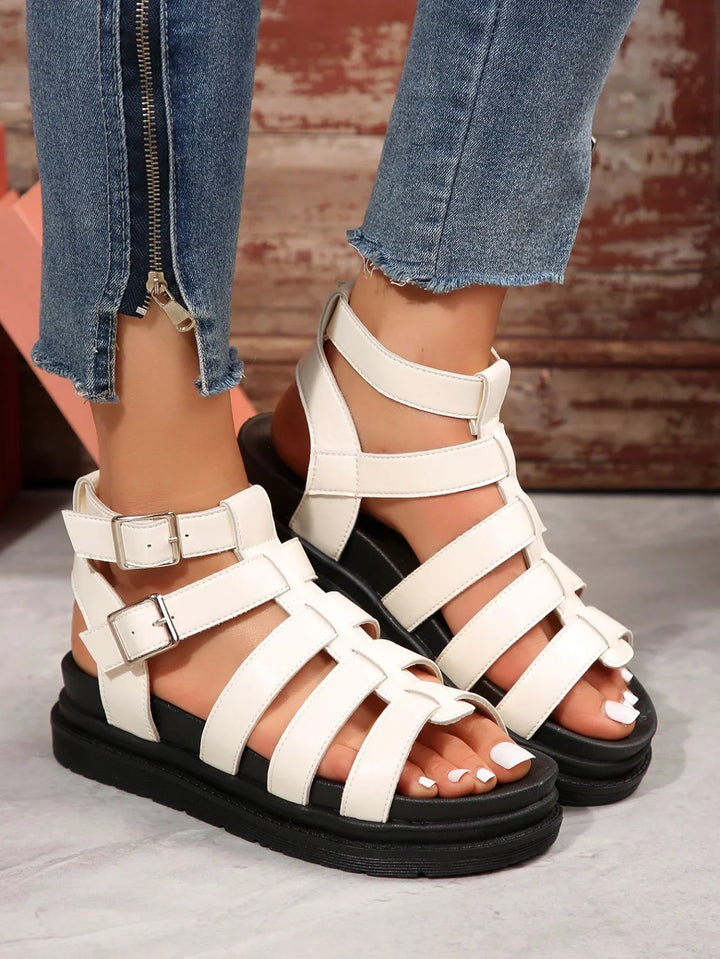 White strappy leather gladiator sandals with buckles on feet wearing blue denim jeans with zipper detail