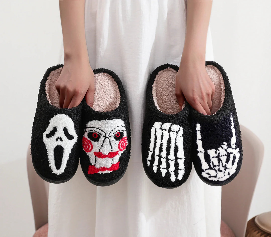 Hands holding black cozy slippers with horror and skeleton designs, soft fleece interior