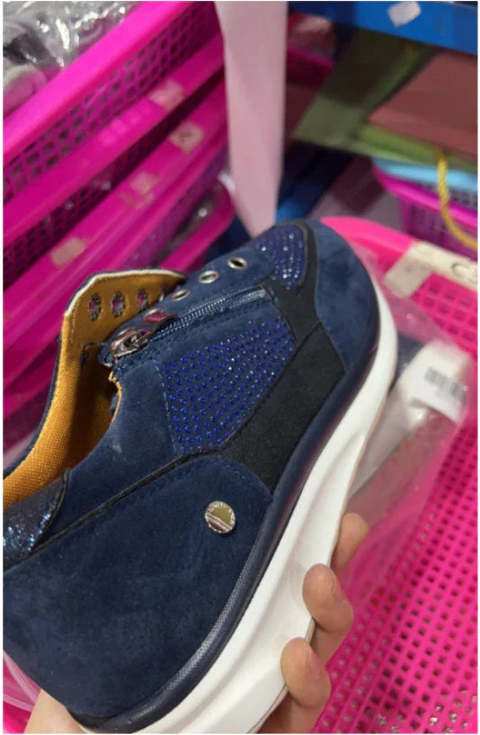 Hand holding a navy blue sneaker with blue rhinestones and a white sole, photographed over pink storage baskets.