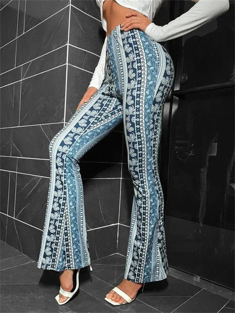 Woman wearing high-waisted blue patterned flare pants with white open-toe heels against dark tile wall
