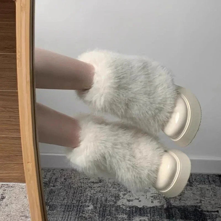 White fluffy fur slippers with thick soles worn indoors on carpeted floor