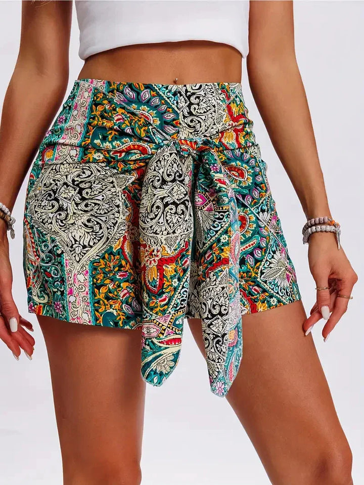 Woman wearing vibrant high-waisted bohemian print shorts with front tie detail and white crop top