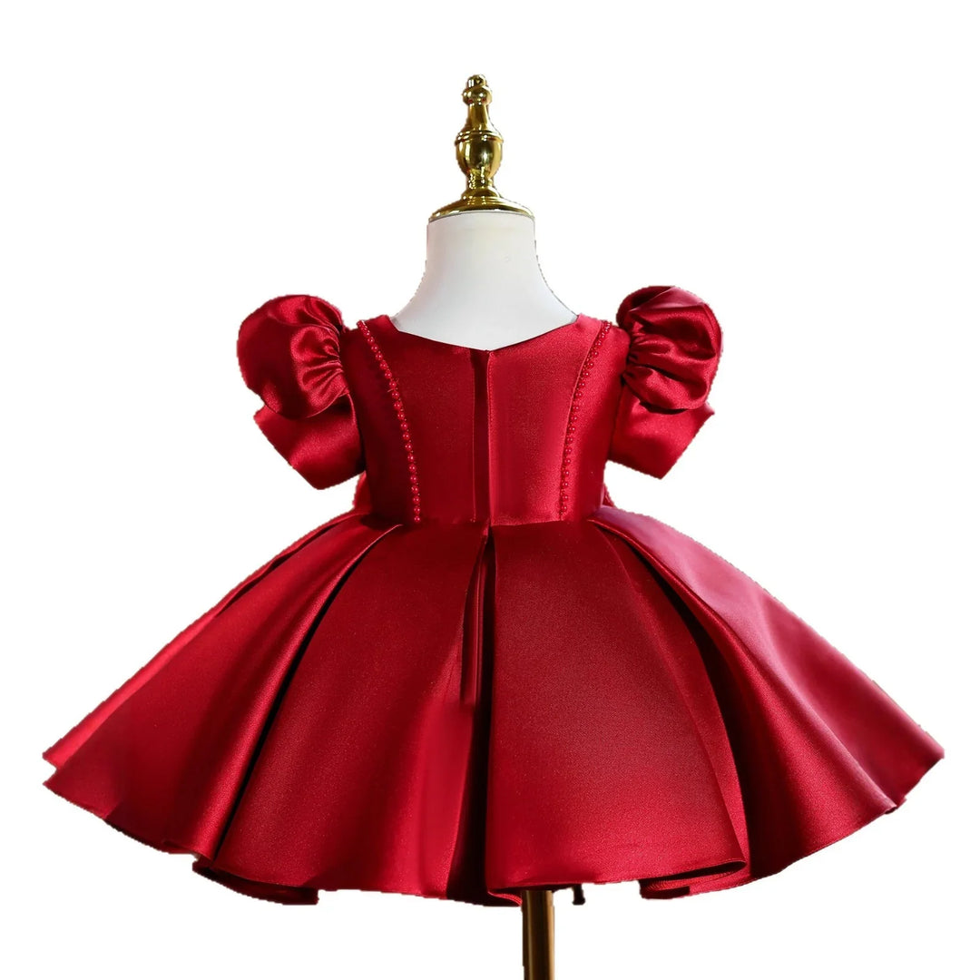 Elegant red satin baby dress with puff sleeves and pleated skirt on mannequin