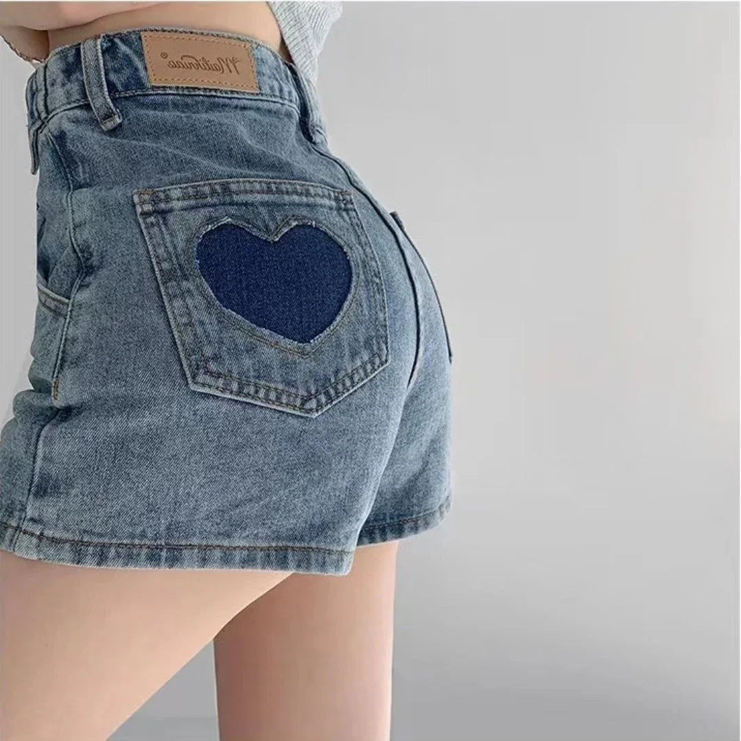 Close-up of high-waisted blue denim shorts with a dark heart-shaped patch on back pocket