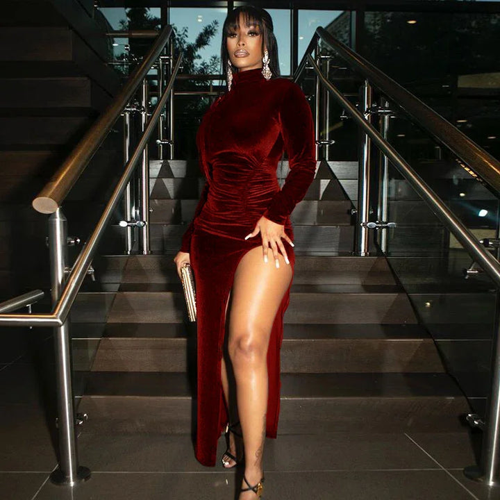 Woman in a burgundy velvet dress with thigh-high slit standing on modern staircase with glass railings