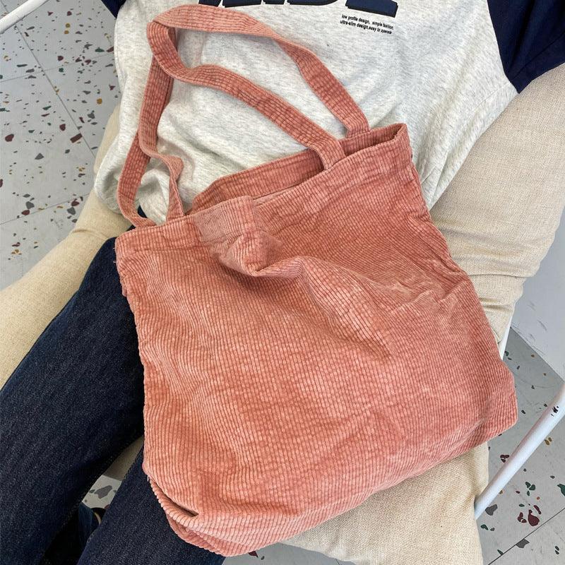 Soft pink corduroy tote bag resting on a person's lap wearing jeans and a light gray T-shirt