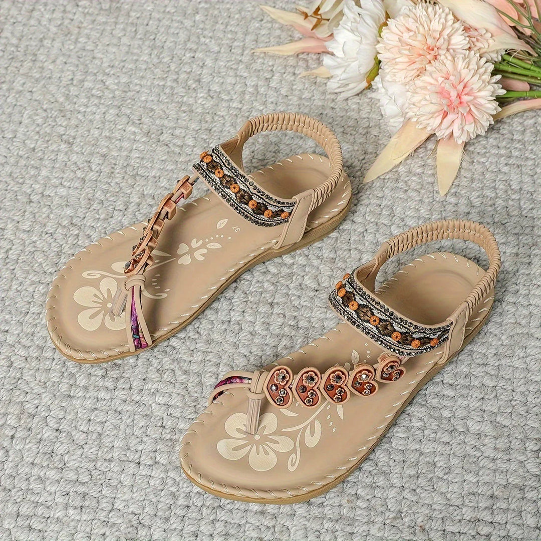 Pair of beige floral sandals with ankle straps and decorative beads on gray carpet