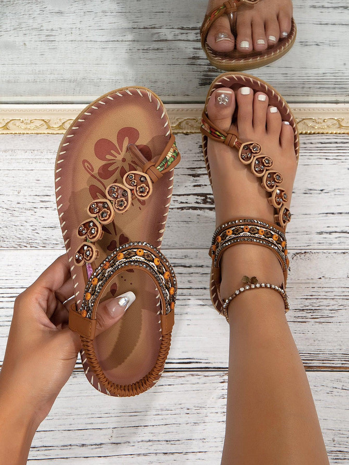 Brown embellished thong sandals with floral details worn on foot against white wooden background