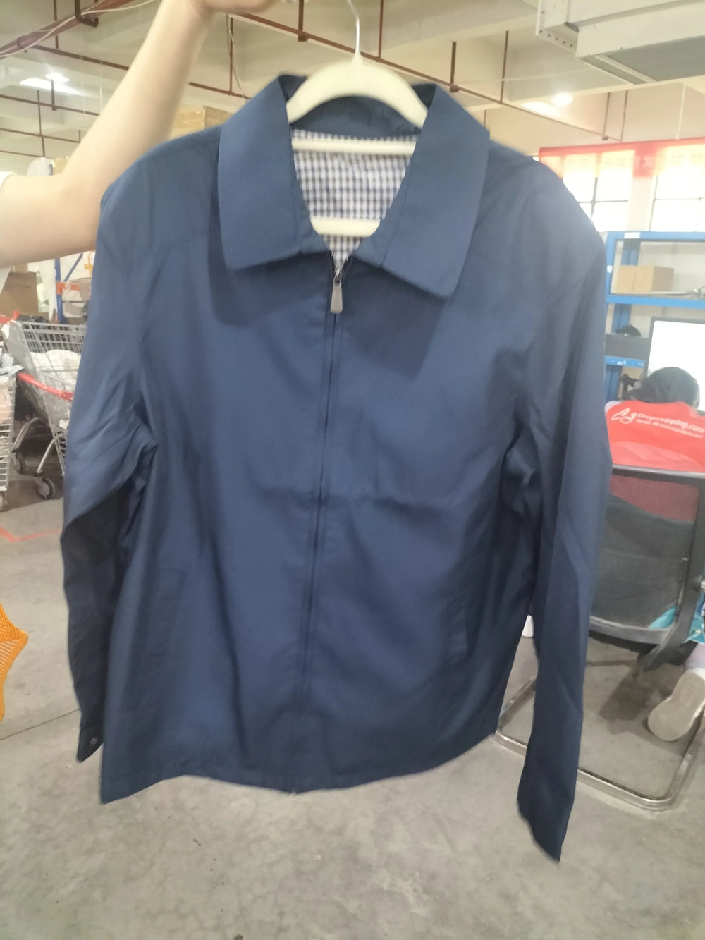 Navy blue zip-up jacket with checkered inner lining, held on a hanger in a warehouse