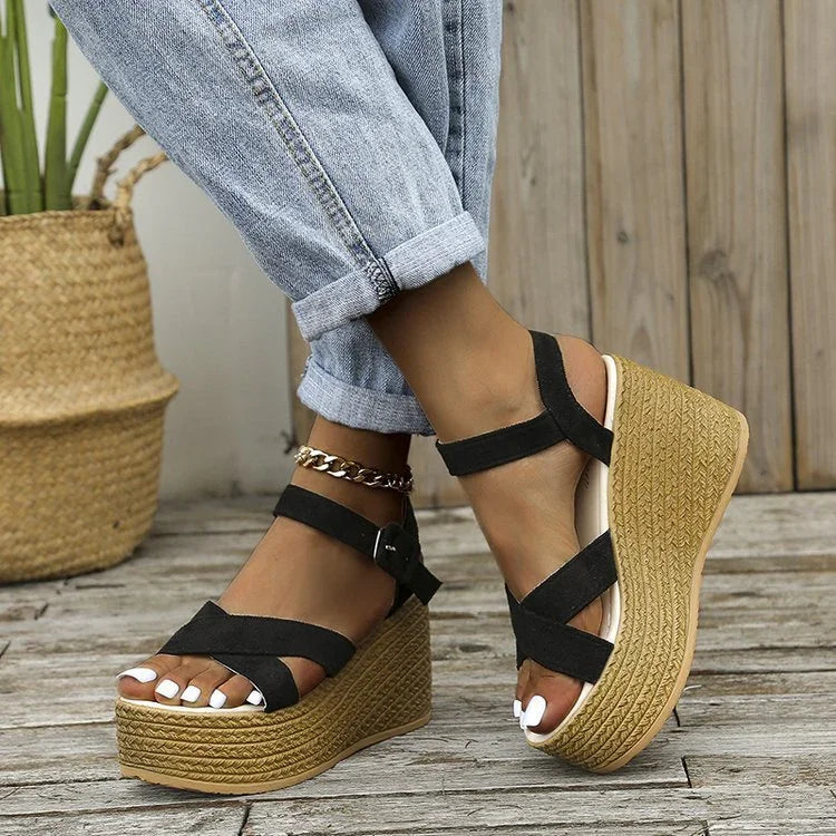 Woman wearing black strappy platform wedge sandals with light blue rolled-up jeans on wooden floor