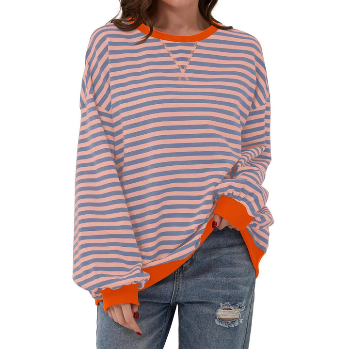 Woman wearing loose striped long sleeve sweatshirt with orange cuffs and hem paired with ripped jeans