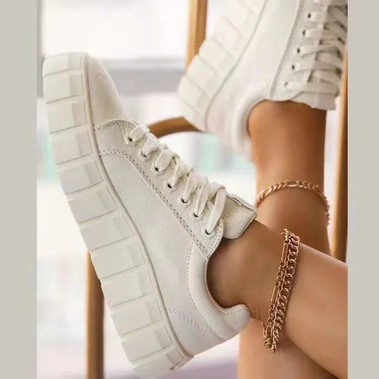 White platform sneakers worn with gold chain anklets on a seated person's legs