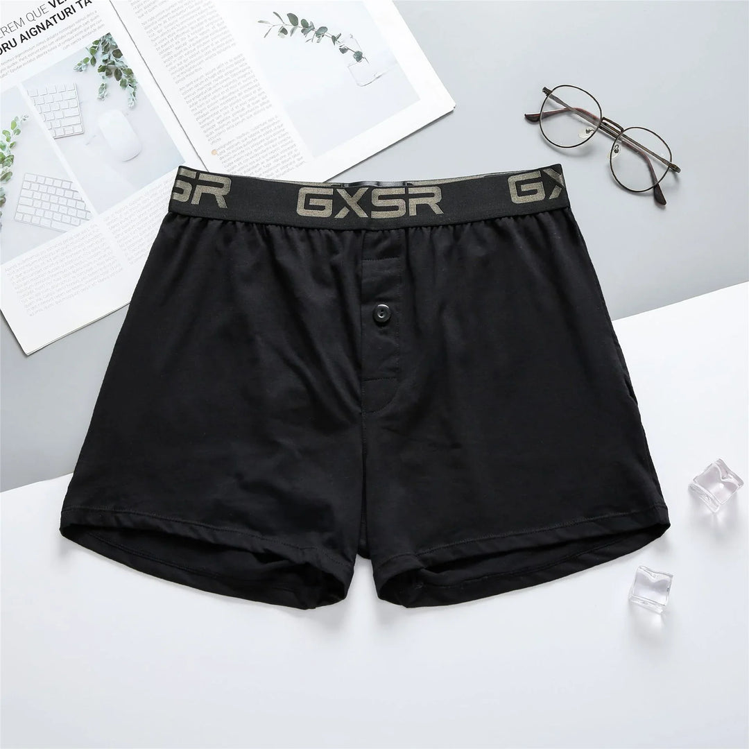 Black men's boxer shorts with GXSR waistband, eyeglasses, magazine, and ice cubes on gray and white surface