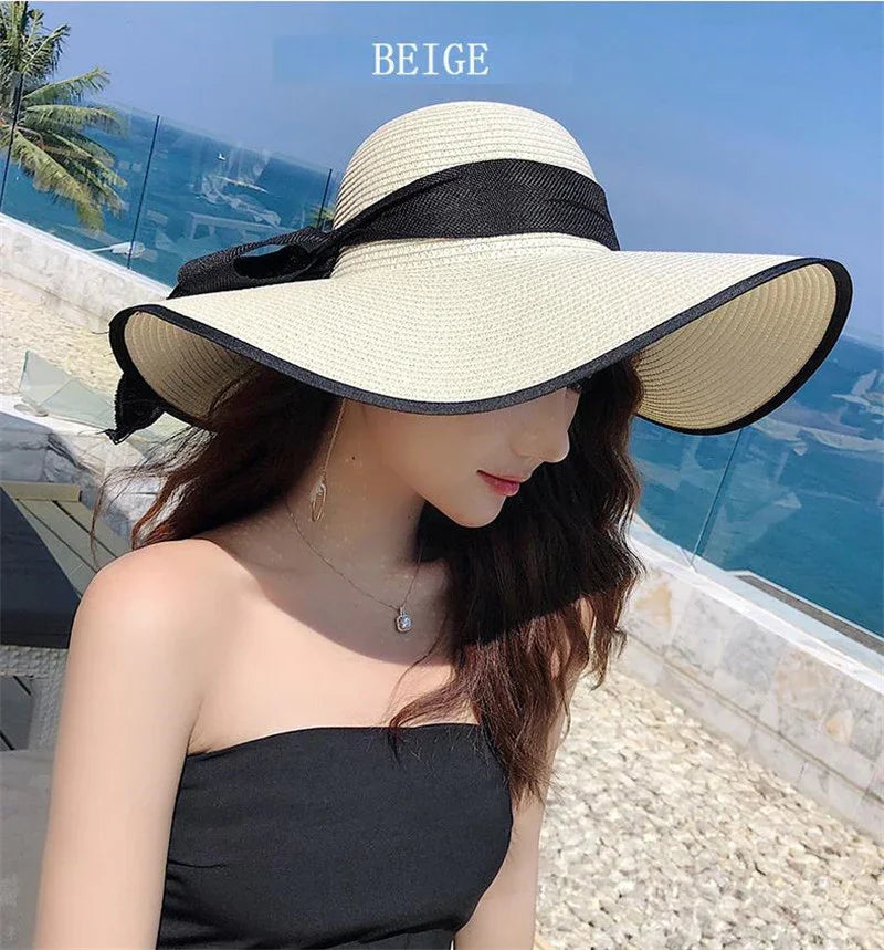 Woman wearing a beige wide-brim sun hat with black trim and bow by the ocean on a sunny day