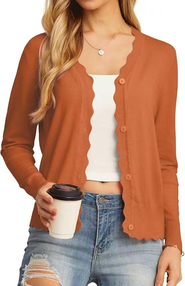 Woman in orange scalloped cardigan, white crop top, distressed blue jeans holding coffee cup
