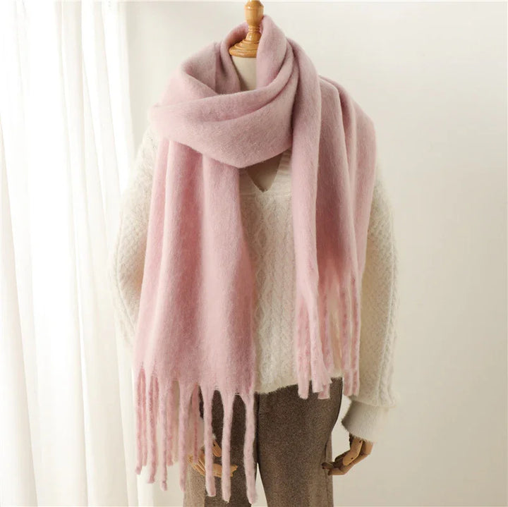Soft pink fringed scarf draped on mannequin wearing cream knit sweater and brown pants