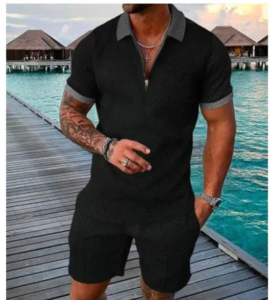 Man wearing black short-sleeve knit shirt and shorts on wooden pier with turquoise sea and overwater bungalows