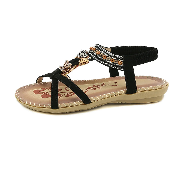 Black flat sandal with beaded and floral decorations on straps and cushioned tan sole